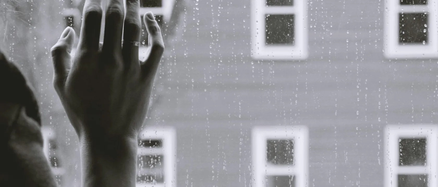 Photo of a hand on a window pane with rain outside