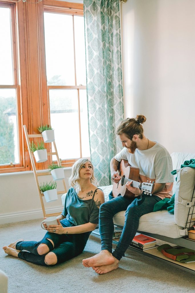 Scène de vie avec un couple qui se trouve dans une pièce d'une maison. Un homme joue de la guitar.